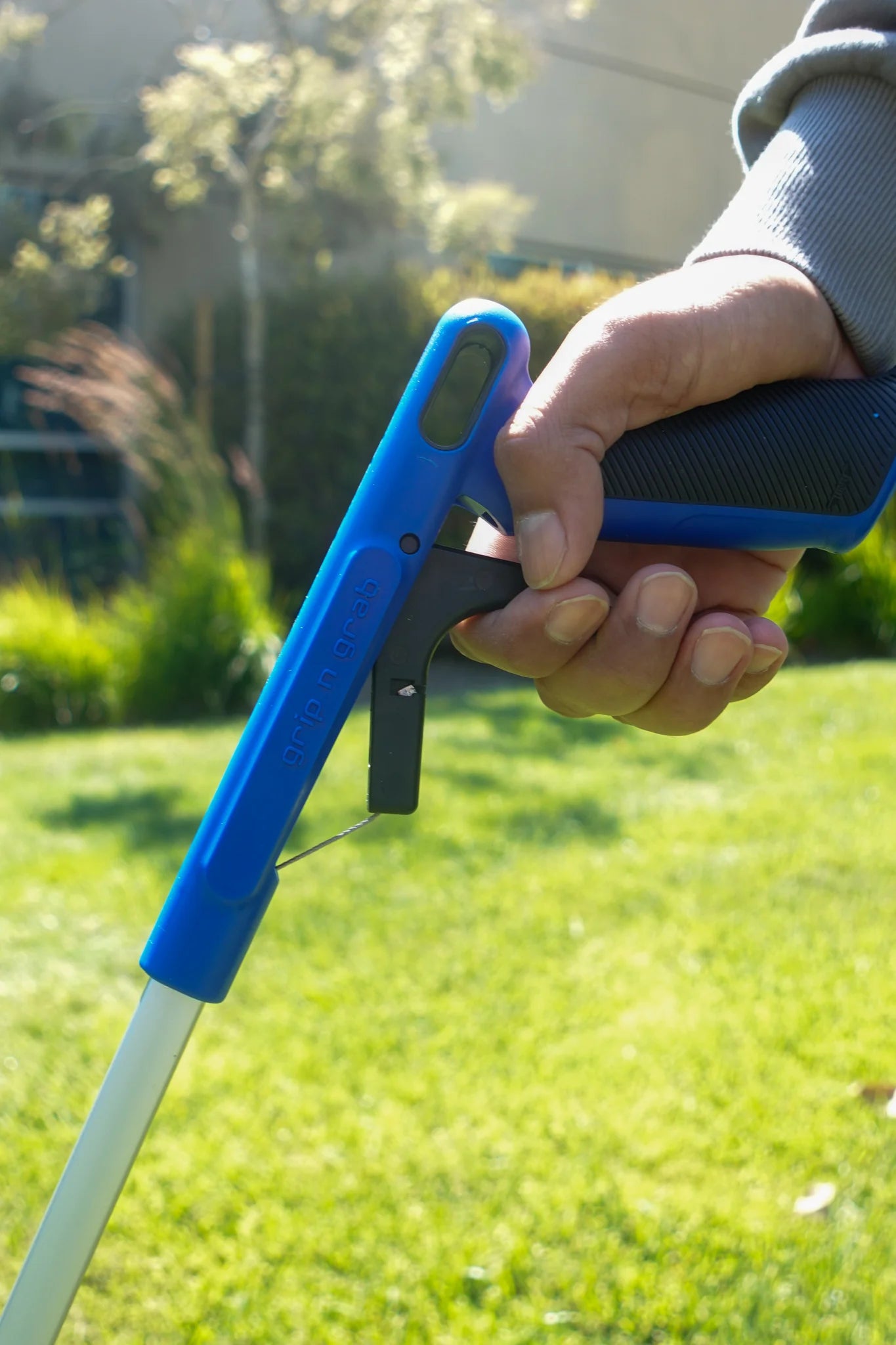 Hand holding a blue and black Grip and Grab tool against a grassy background