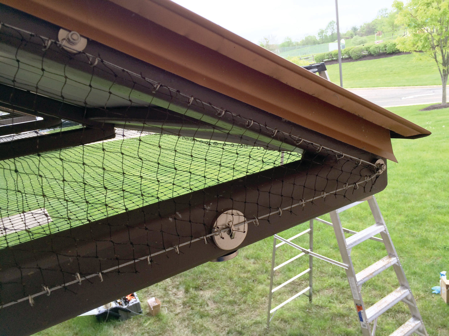 Gutter guard installation on a roof with a ladder and grassy area in the background