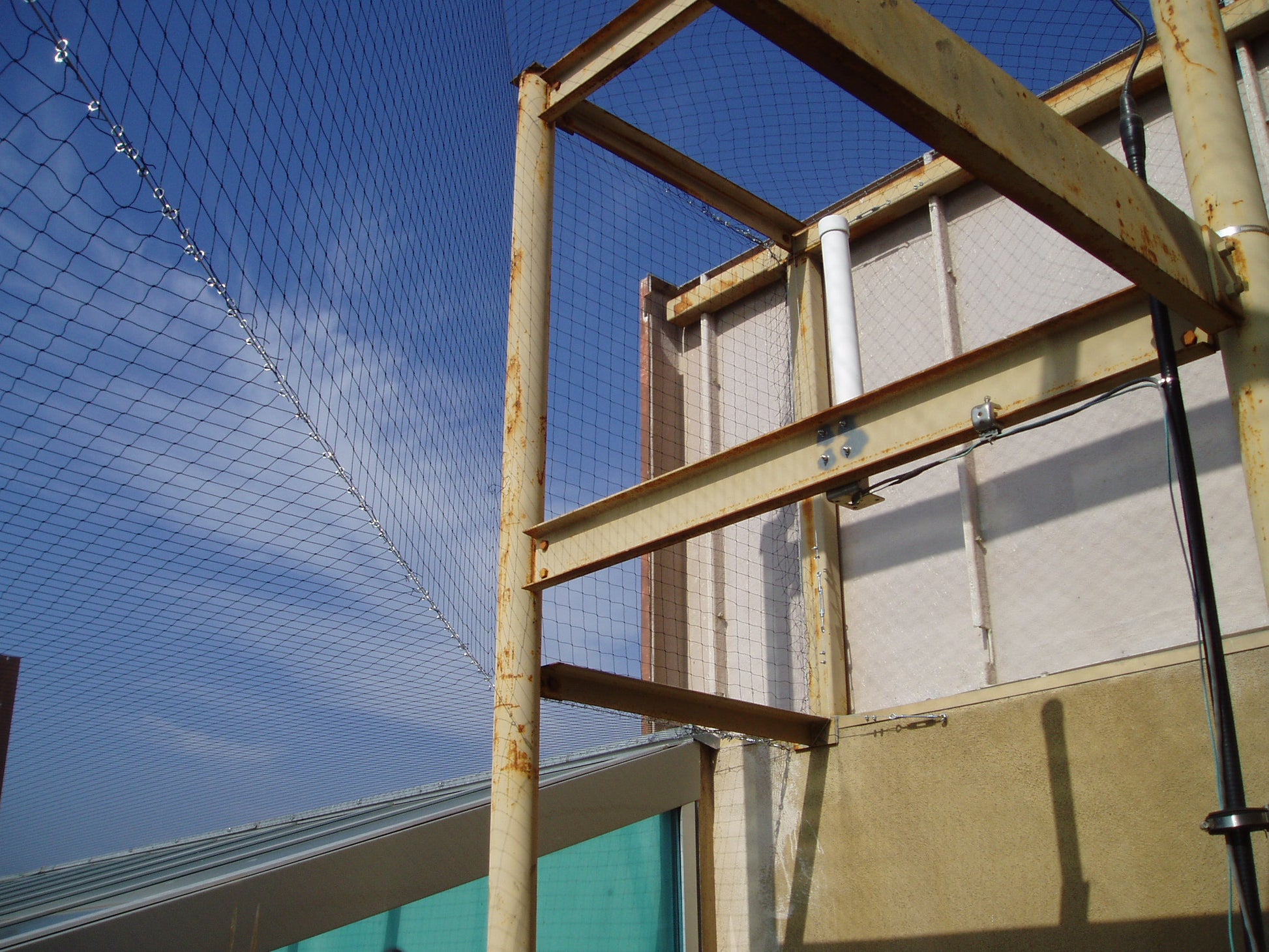 Rust-colored metal structure with a blue sky and Bird barrier netting in the background