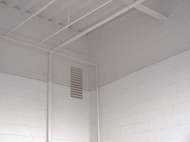 Ceiling with a bird barrier net and a vent in a room with white walls.